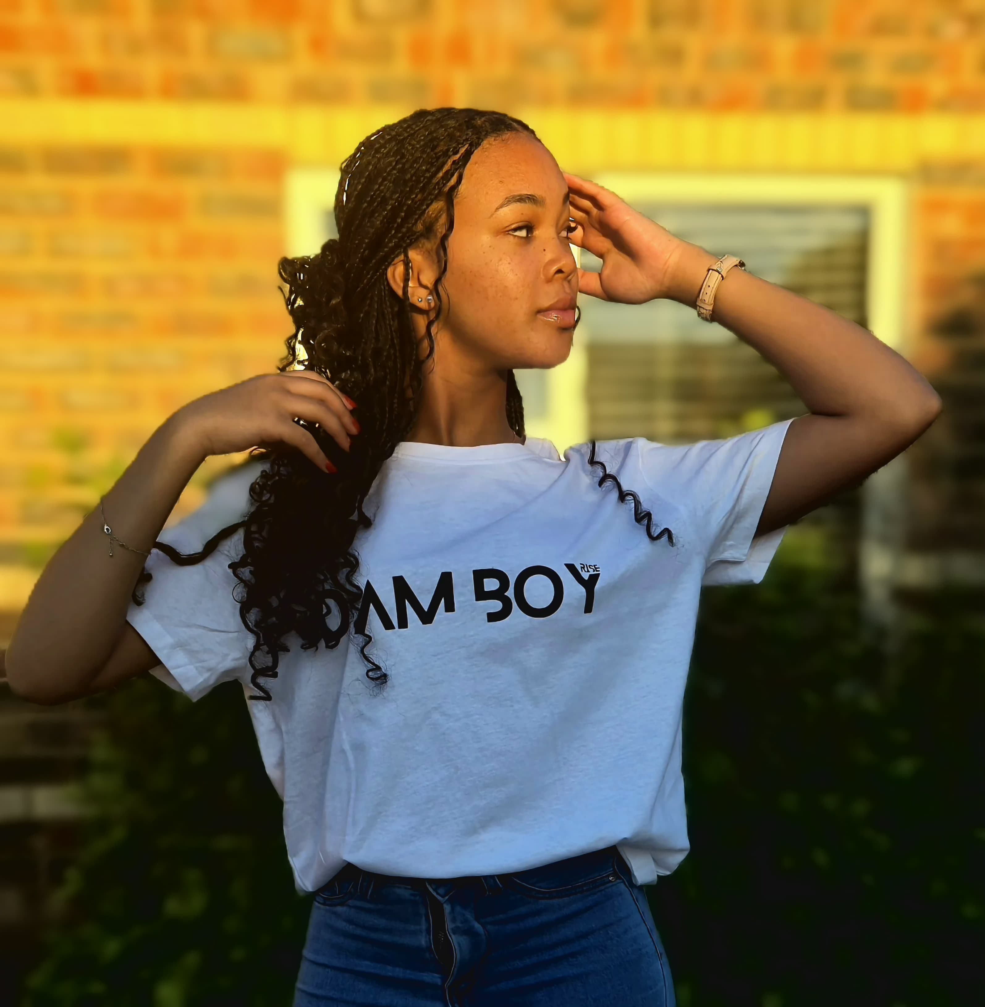Person wearing a white t-shirt with text, standing outdoors against a brick wall.